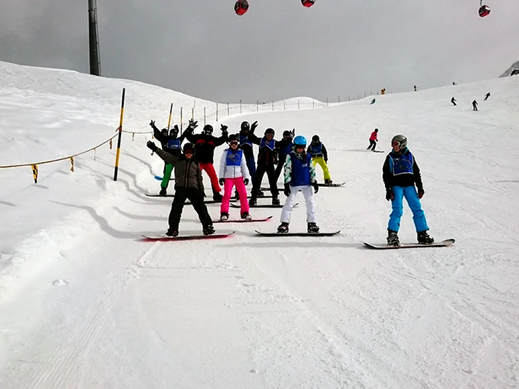 Gruppe mit Snowboards steht am Pistenrand.